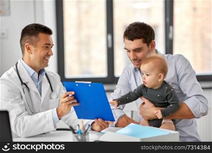 medicine, healthcare, pediatry and people concept - happy doctor showing clipboard to father with baby daughter at medical office in hospital. father with baby and doctor at clinic