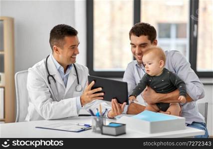 medicine, healthcare, pediatry and people concept - happy doctor showing tablet computer to father with baby daughter at medical office in hospital. father with baby and doctor with tablet at clinic