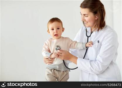 medicine, healthcare, pediatry and people concept - happy doctor with stethoscope listening to baby on medical exam at clinic. happy doctor with stethoscope and baby at clinic