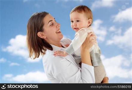 medicine, healthcare, pediatry and people concept - happy woman doctor or pediatrician holding baby over blue sky background. happy doctor or pediatrician with baby over sky