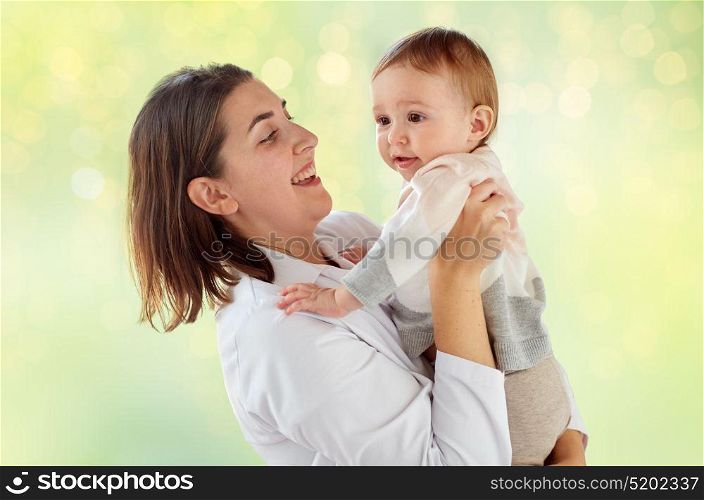 medicine, healthcare, pediatry and people concept - happy woman doctor or pediatrician holding baby over green lights background. happy woman doctor or pediatrician with baby
