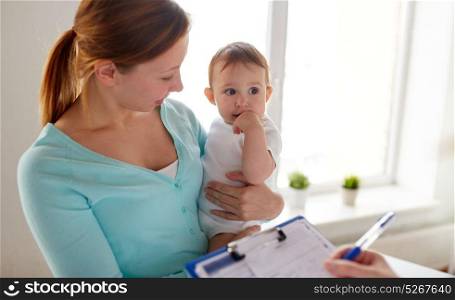 medicine, healthcare, pediatry and people concept - happy woman with baby and doctor with clipboard at clinic. happy woman with baby and doctor at clinic