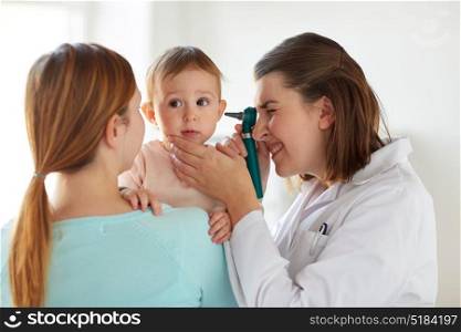 medicine, healthcare, pediatry and people concept - otolaryngologist or doctor checking baby ear with otoscope and young woman at clinic. doctor with otoscope checking baby ear at clinic