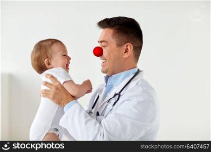 medicine, healthcare, pediatry and red nose day concept - happy doctor or pediatrician holding baby on medical exam at clinic. happy baby at doctor on red nose day