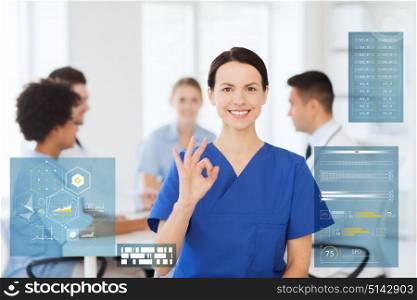 medicine, healthcare, technology and people concept - happy female doctor over group of medics meeting at hospital showing ok hand sign. happy doctor at hospital showing ok hand sign
