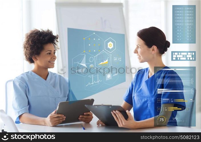 medicine, healthcare, technology and people concept - happy female doctors with tablet pc computer and clipboard meeting at medical office. doctors with tablet pc and clipboard at hospital
