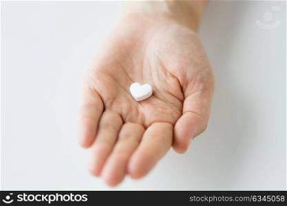 medicine, nutritional supplements and people concept - close up of hand holding pill in shape of heart. close up of hand holding medicine heart pill