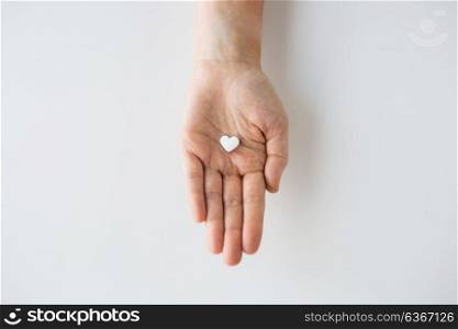 medicine, nutritional supplements and people concept - close up of hand holding pill in shape of heart. close up of hand holding medicine heart pill