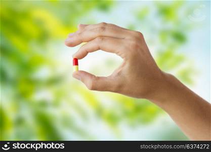medicine, nutritional supplements and people concept - close up of hand holding capsule of drug over green natural background. close up of hand holding capsule of medicine