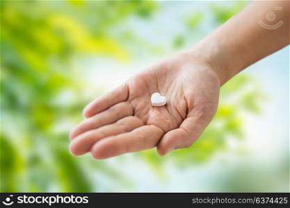 medicine, nutritional supplements and people concept - close up of hand holding pill in shape of heart over green natural background. close up of hand holding medicine heart pill