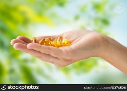 medicine, nutritional supplements and people concept - close up of hand holding cod liver oil capsules over green natural background. hand holding cod liver oil capsules