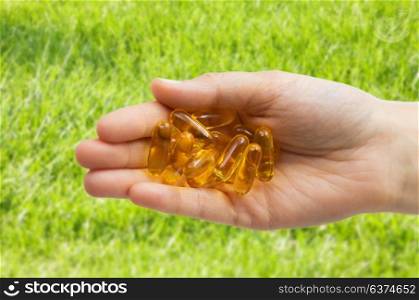 medicine, nutritional supplements and people concept - close up of hand holding cod liver oil capsules over grass background. hand holding cod liver oil capsules