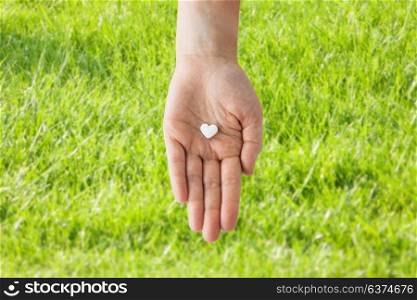 medicine, nutritional supplements and people concept - close up of hand holding pill in shape of heart over grass background. close up of hand holding medicine heart pill