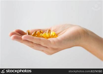 medicine, nutritional supplements and people concept - close up of hand holding cod liver oil capsules. hand holding cod liver oil capsules