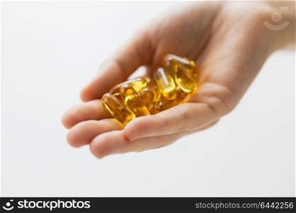 medicine, nutritional supplements and people concept - close up of hand holding cod liver oil capsules. hand holding cod liver oil capsules