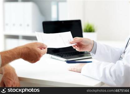 medicine, old age, healthcare and people concept - close up of doctor giving prescription to senior patient at hospital