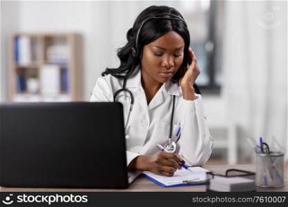 medicine, online service and healthcare concept - african american female doctor or nurse with headset, clipboard and laptop at hospital. doctor with headset and clipboard at hospital