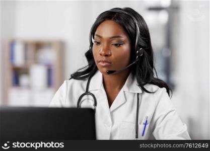 medicine, online service and healthcare concept - african american female doctor or nurse with headset and laptop having conference or video call at hospital. african doctor with headset and laptop at hospital