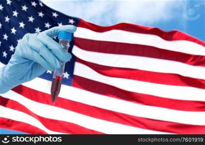 medicine, pandemic and virus concept - close up of hand holding test tube with coronavirus blood test over flag of america background. hand holding test tube with coronavirus blood test