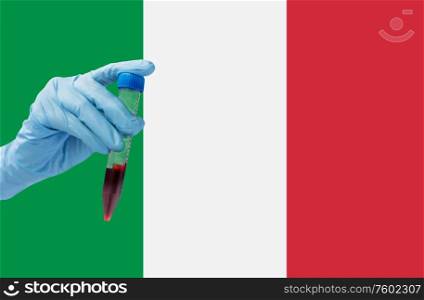 medicine, pandemic and virus concept - close up of hand holding test tube with coronavirus blood test over flag of italy background. hand holding test tube with coronavirus blood test