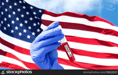 medicine, pandemic and virus concept - close up of hand in protective glove holding test tube with blood sample for coronavirus research over flag of america on background. hand with blood sample in test tube of coronavirus