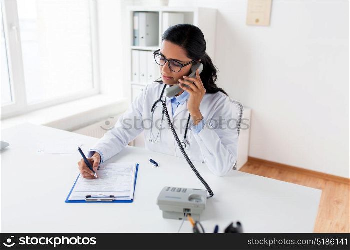 medicine, people and healthcare concept - female doctor with medical report on clipboard calling on phone at hospital. doctor with clipboard calling on phone at hospital