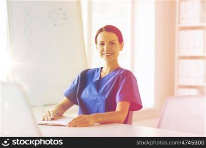 medicine, people and healthcare concept - happy female doctor or nurse writing medical report to clipboard at hospital