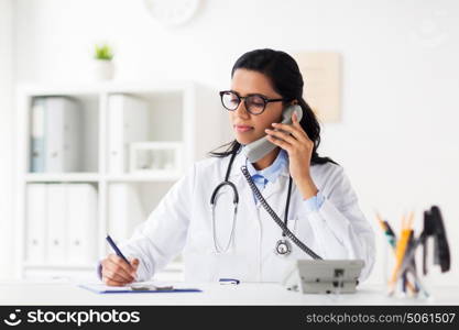 medicine, people and healthcare concept - happy female doctor with papers and clipboard calling on phone at hospital. doctor with clipboard calling on phone at hospital