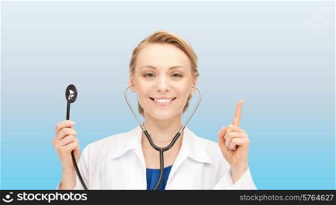medicine, people, profession and healthcare concept - smiling young female doctor in white coat holding stethoscope and pointing finger up over blue background