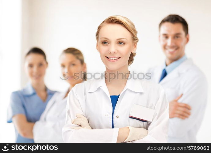 medicine, people, profession and teamwork concept - smiling young female doctor in white coat over group of medics in hospital