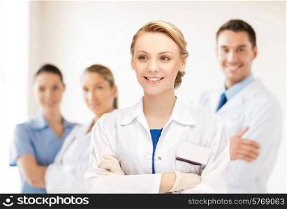 medicine, people, profession and teamwork concept - smiling young female doctor in white coat over group of medics in hospital