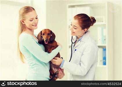 medicine, pet, animal, health care and people concept - happy woman holding dachshund and veterinarian doctor with stethoscope at vet clinic