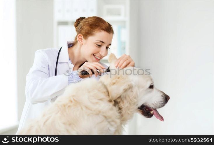 medicine, pet, animals, health care and people concept - happy veterinarian doctor with otoscope checking up golden retriever dog ear at vet clinic