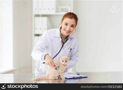medicine, pet, animals, health care and people concept - happy veterinarian doctor with stethoscope checking scottish fold kitten up at vet clinic