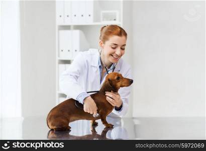 medicine, pet, animals, health care and people concept - happy veterinarian doctor with stethoscope examining dachshund dog at vet clinic