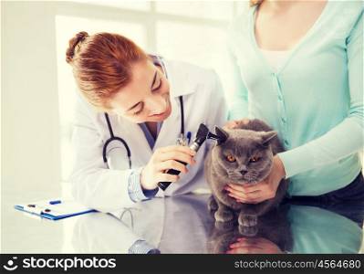 medicine, pet, animals, health care and people concept - happy woman and veterinarian doctor with otoscope checking up british cat ear at vet clinic