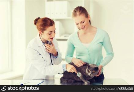 medicine, pet, animals, health care and people concept - happy woman and veterinarian doctor with stethoscope checking british cat up at vet clinic