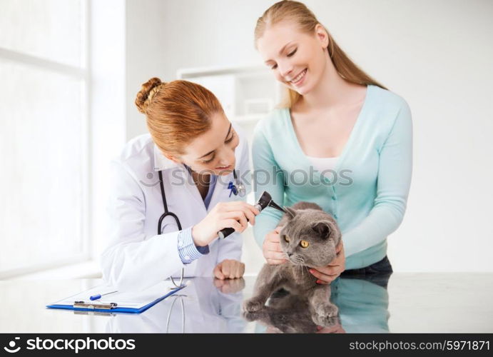 medicine, pet, animals, health care and people concept - happy woman and veterinarian doctor with otoscope checking up british cat ear at vet clinic