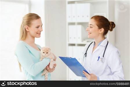 medicine, pet, animals, health care and people concept - happy woman holding scottish fold kitten and veterinarian doctor with clipboard at vet clinic