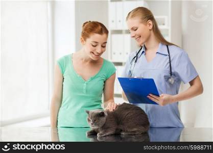 medicine, pet, animals, health care and people concept - happy woman with british cat and veterinarian doctor with clipboard taking notes at vet clinic