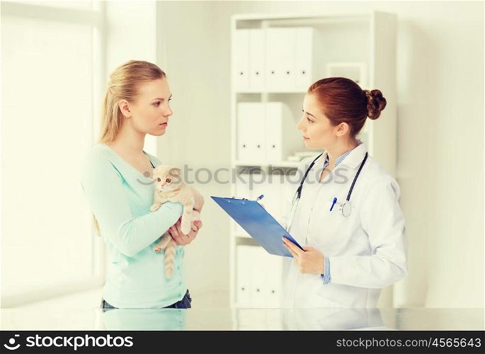 medicine, pet, animals, health care and people concept - woman holding scottish fold kitten and veterinarian doctor with clipboard at vet clinic