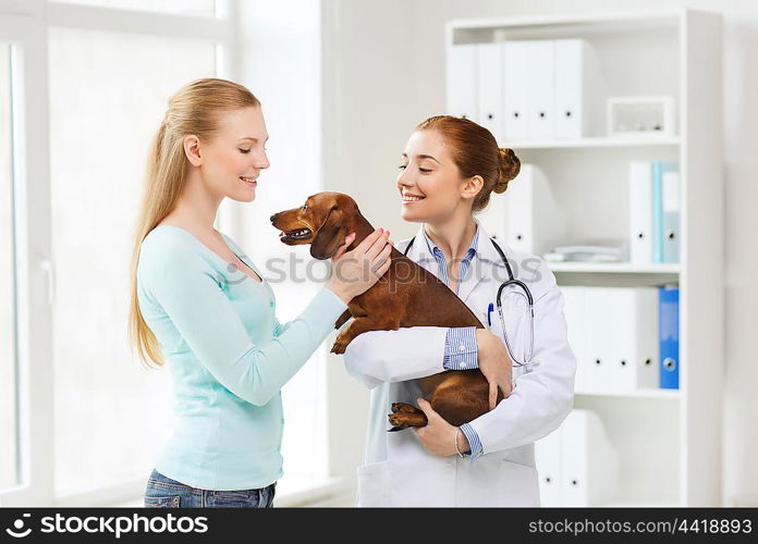 medicine, pet care and people concept - happy woman and veterinarian doctor holding dachshund dog at vet clinic