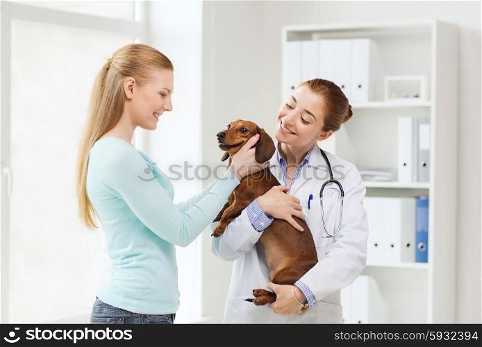 medicine, pet care and people concept - happy woman and veterinarian doctor holding dachshund dog at vet clinic
