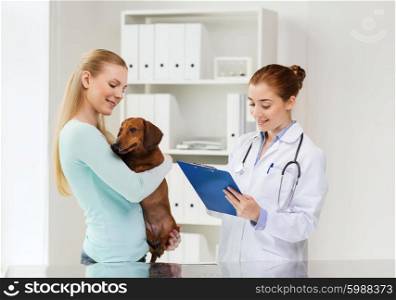medicine, pet care and people concept - happy woman holding dachshund dog and veterinarian doctor with clipboard at vet clinic