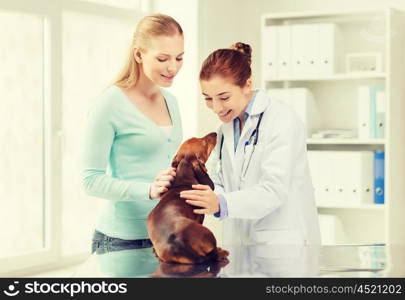 medicine, pet care and people concept - happy woman with dachshund dog and veterinarian doctor at vet clinic