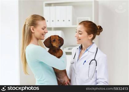 medicine, pet care and people concept - happy woman with dachshund dog and veterinarian doctor at vet clinic