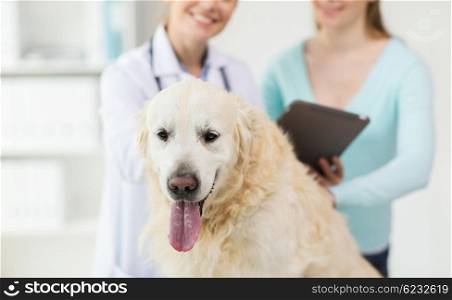 medicine, pet, health care, technology and people concept - close up of happy woman with golden retriever dog and veterinarian doctor holding tablet pc computer at vet clinic