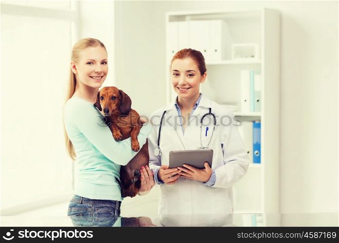 medicine, pet, health care, technology and people concept - happy woman holding dachshund dog and veterinarian doctor with tablet pc computer at vet clinic