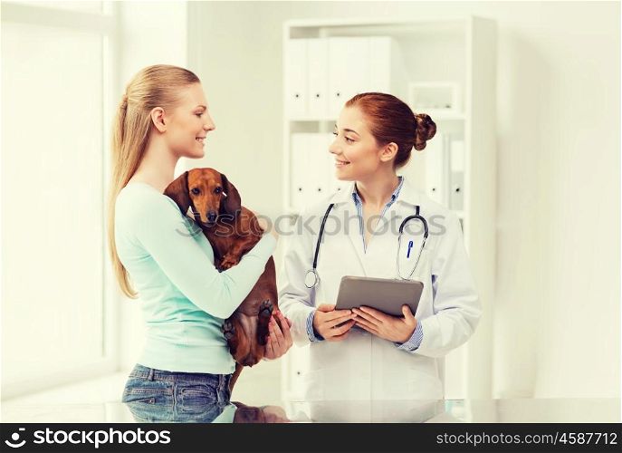 medicine, pet, health care, technology and people concept - happy woman holding dachshund dog and veterinarian doctor with tablet pc computer talking at vet clinic
