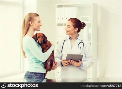 medicine, pet, health care, technology and people concept - happy woman holding dachshund dog and veterinarian doctor with tablet pc computer talking at vet clinic